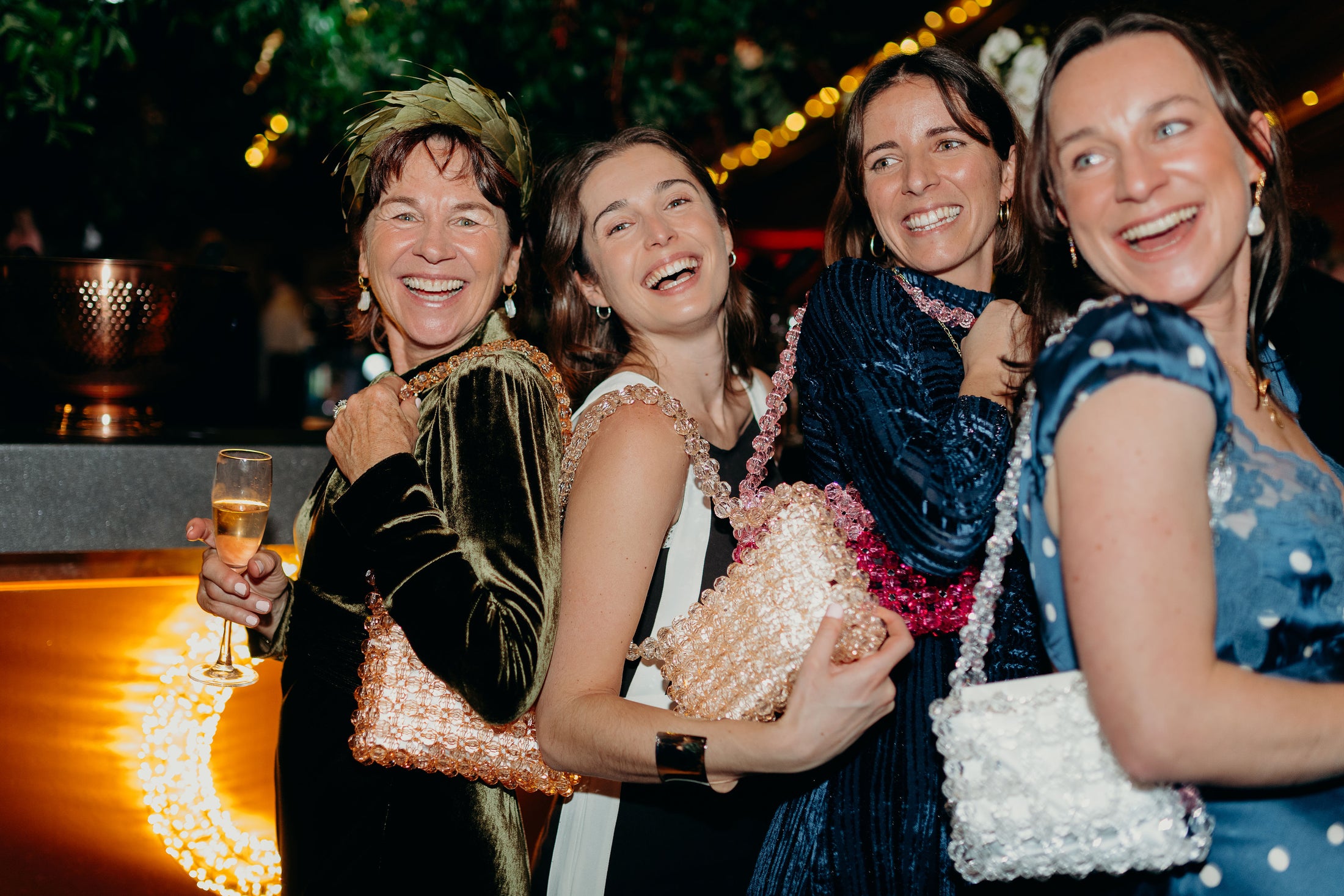 Four women laughing together at a social event with festive decorations wearing bridal bag