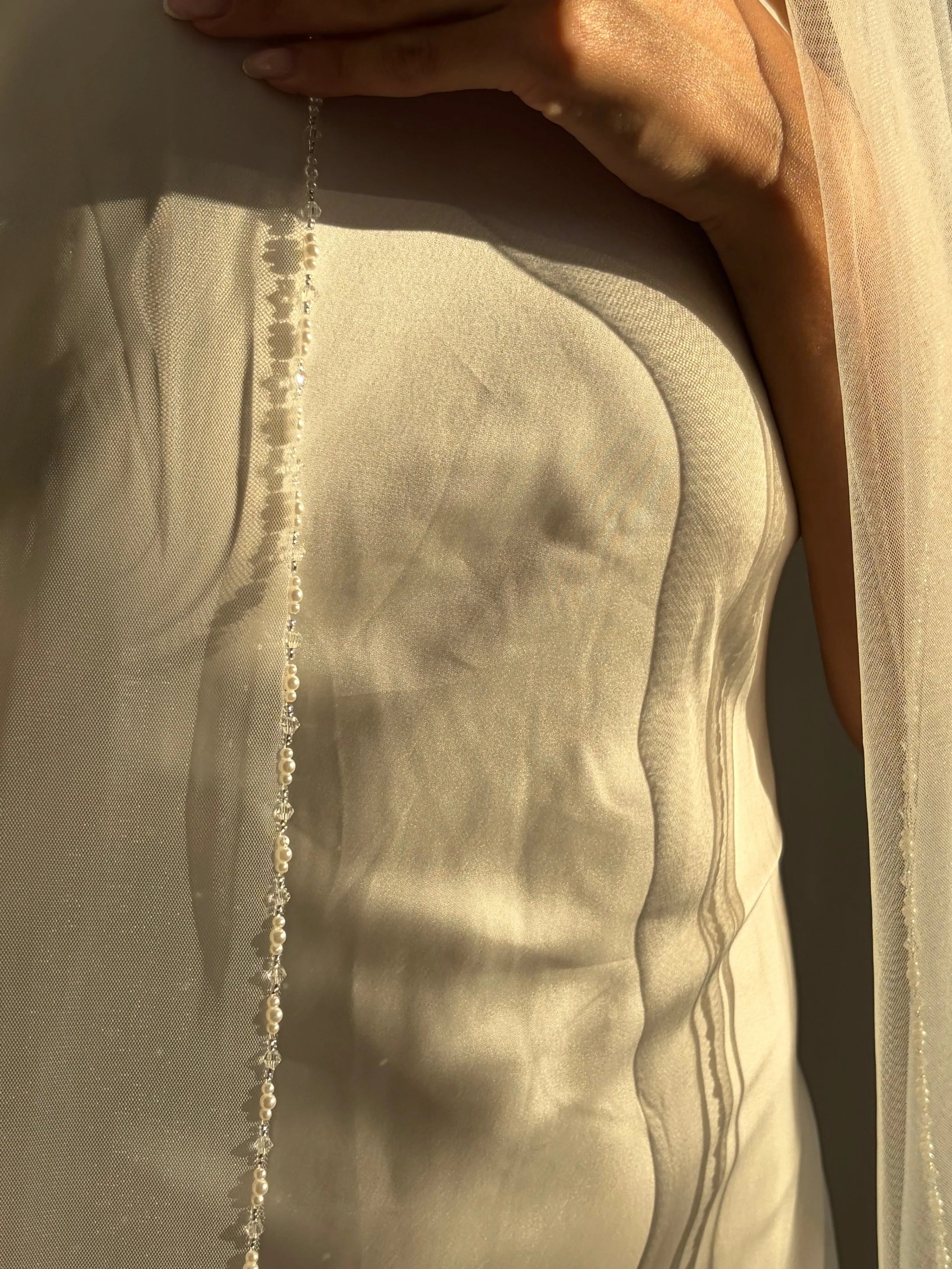close up of person wearing a pearl trim veil and white dress