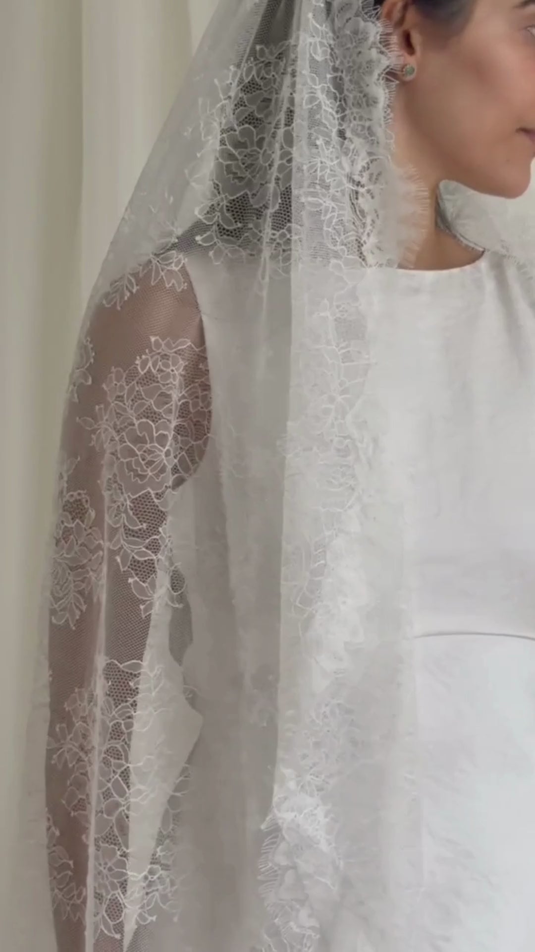 Woman wearing a white lace veil and wedding dress against a white curtain background