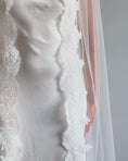 Load and play video in Gallery viewer, A woman in a white wedding dress and long sheer veil with lace trim stands in profile in a room with light wood herringbone flooring and a plain off-white wall.
