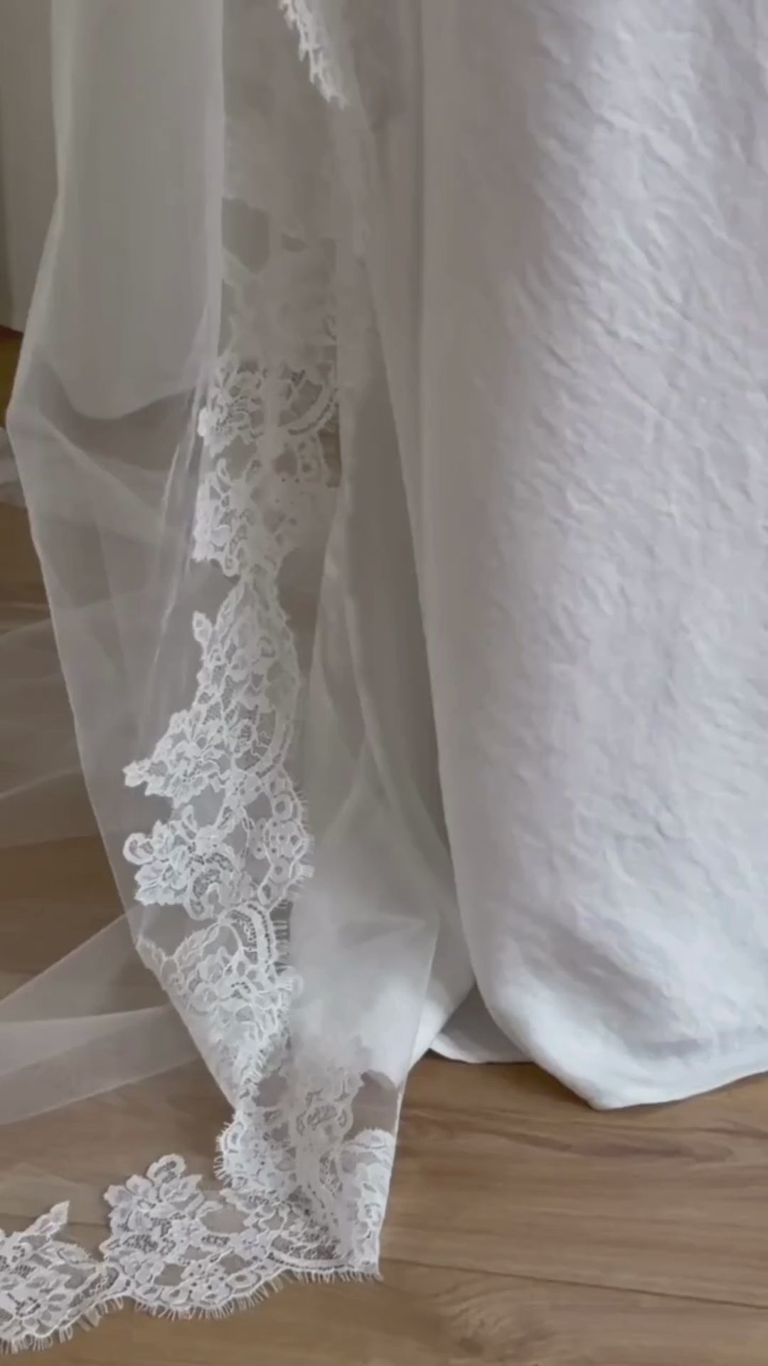 White wedding dress with a long lace veil in front of a white curtain.