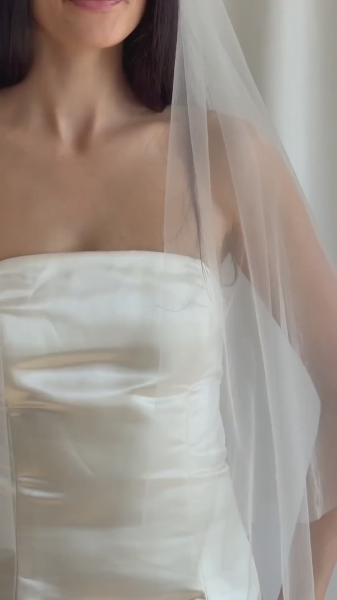 Bride wearing a white wedding dress with a plain veil against a white curtain background.