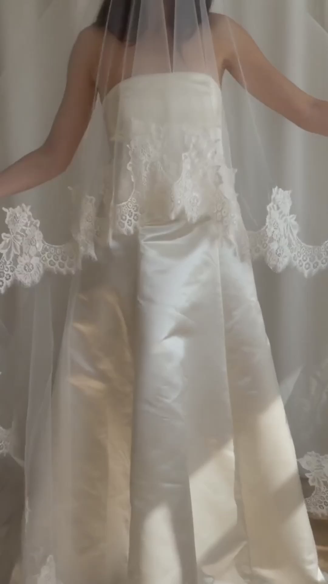 Bride wearing a white wedding dress with a lace veil against a white curtain background.