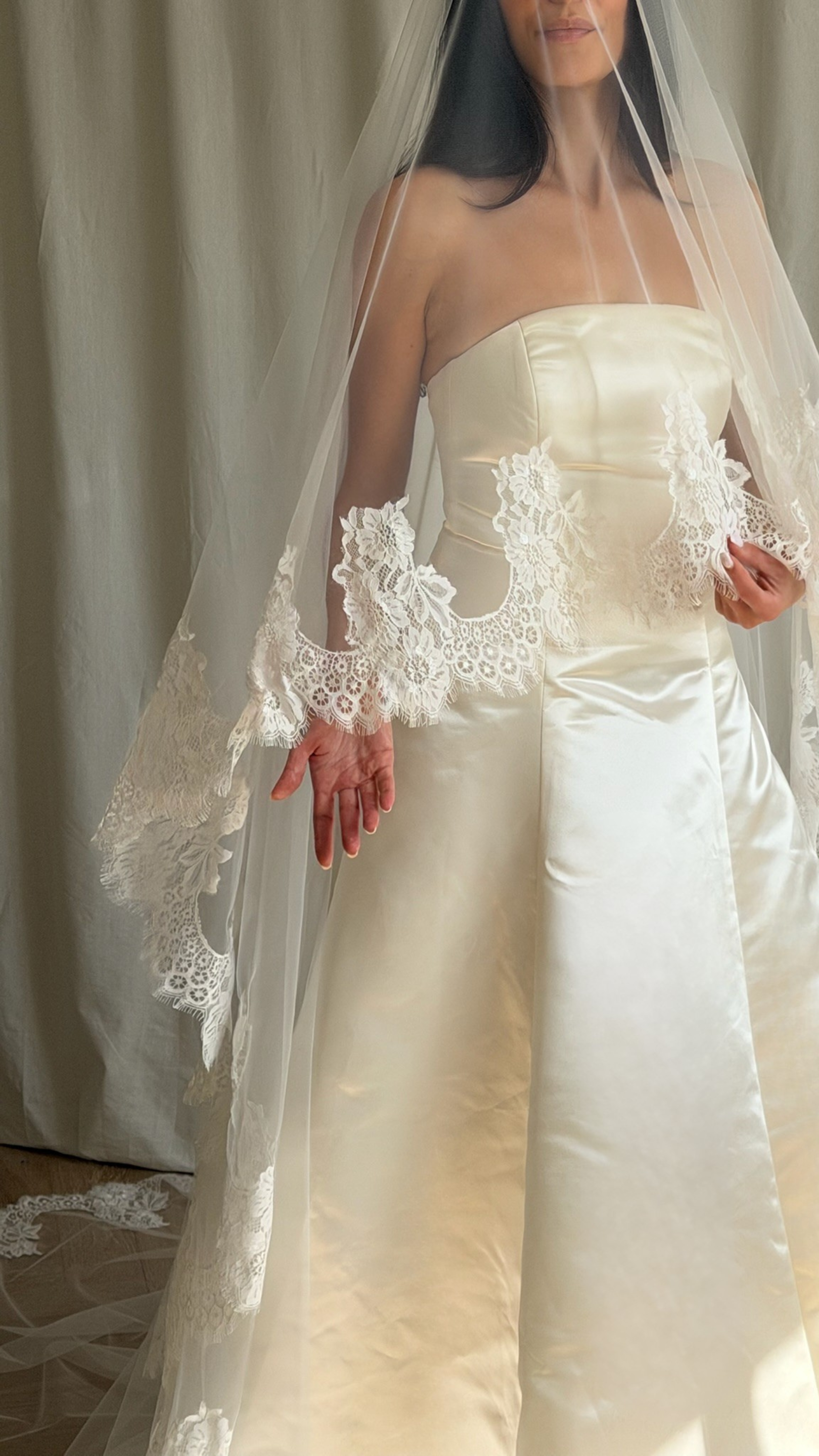 Bride wearing a white wedding dress with a lace veil against a white curtain background.