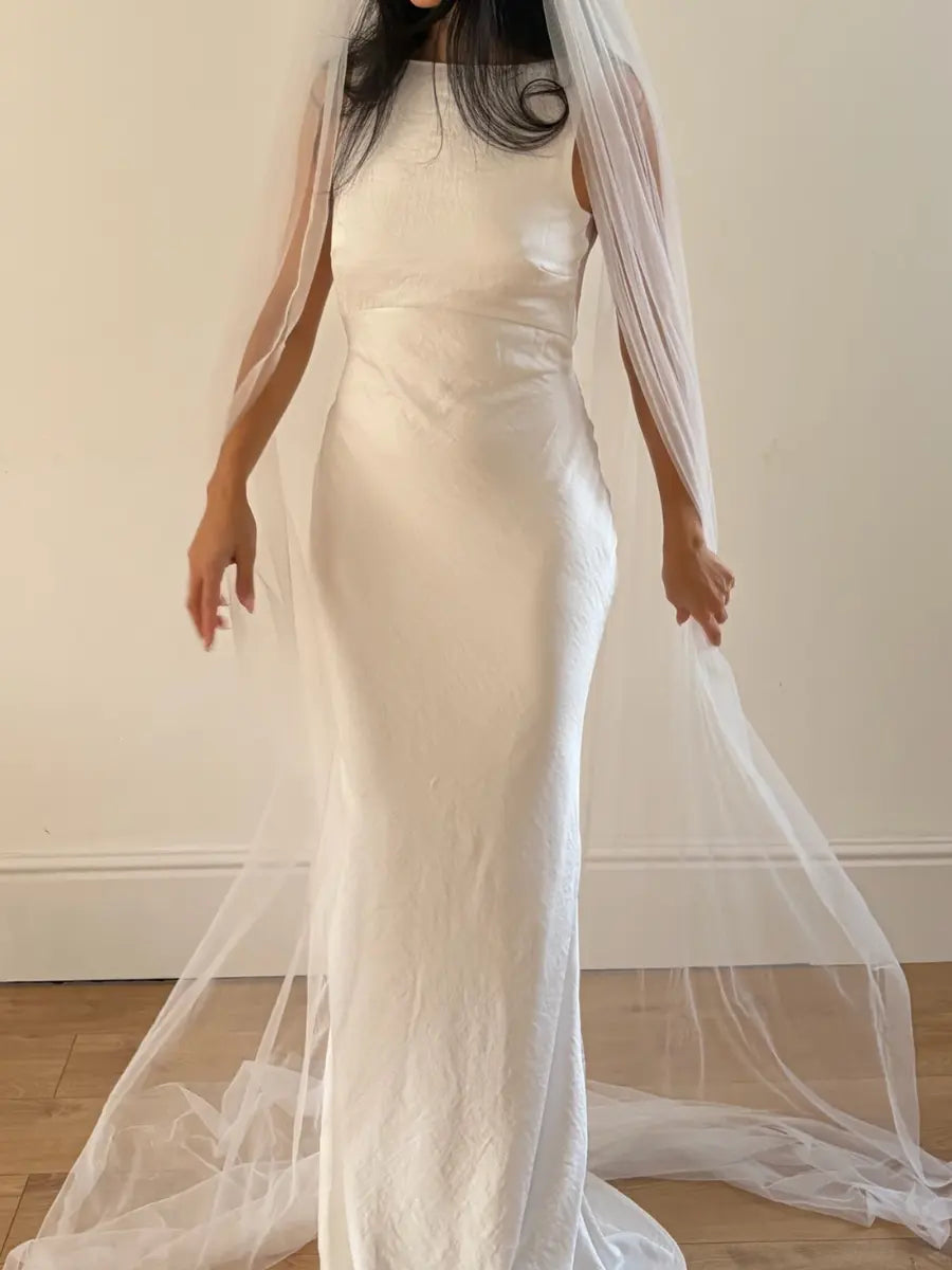 Person wearing a white wedding dress with a long plain veil against a plain background