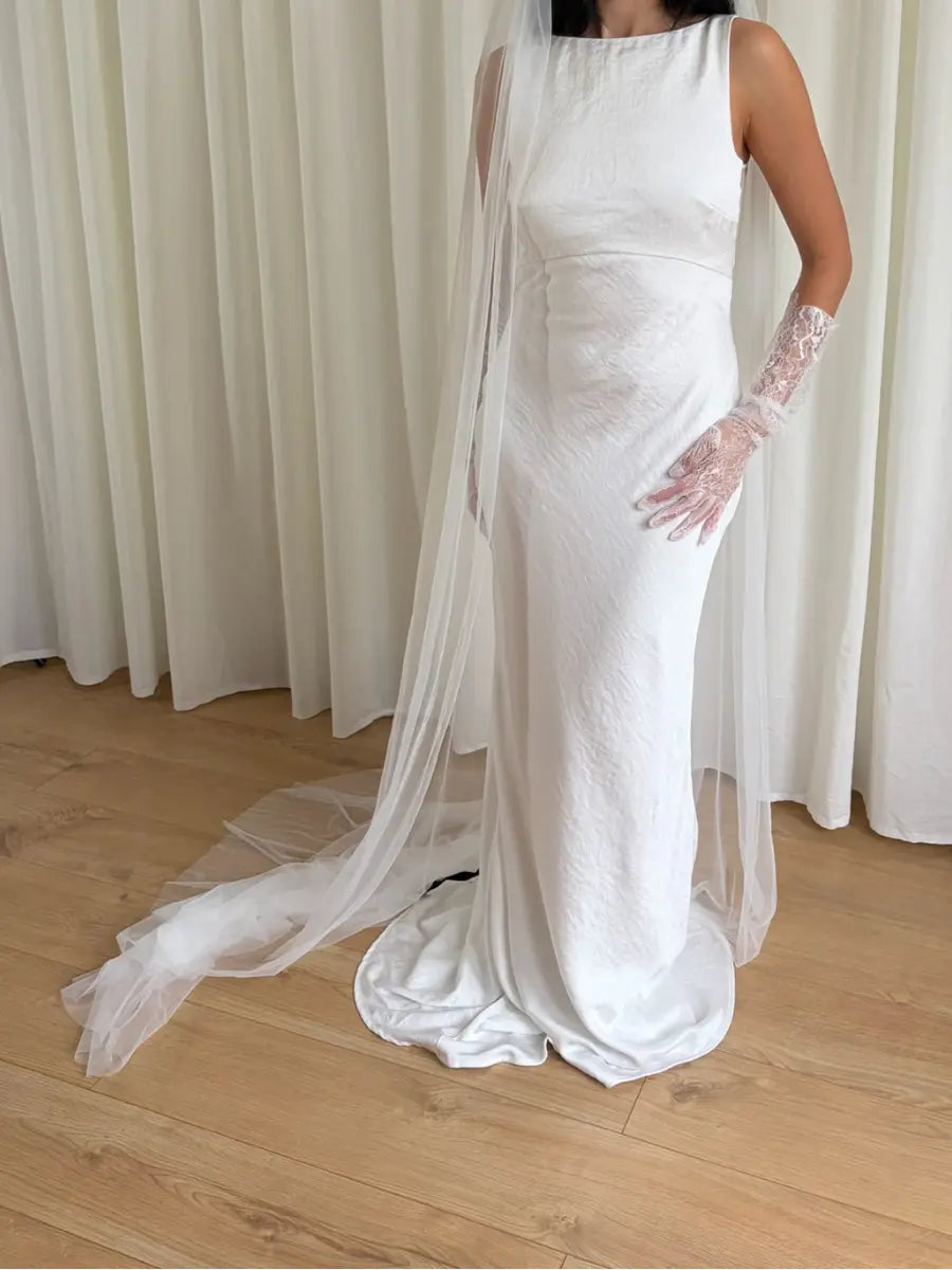 White wedding dress with a plain veil and lace gloves on a wooden floor.