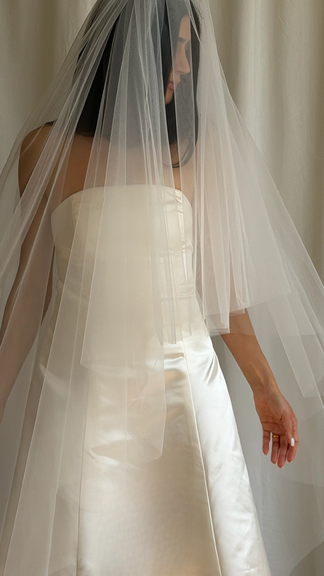 Bride wearing a white strapless gown with a long veil against a neutral background