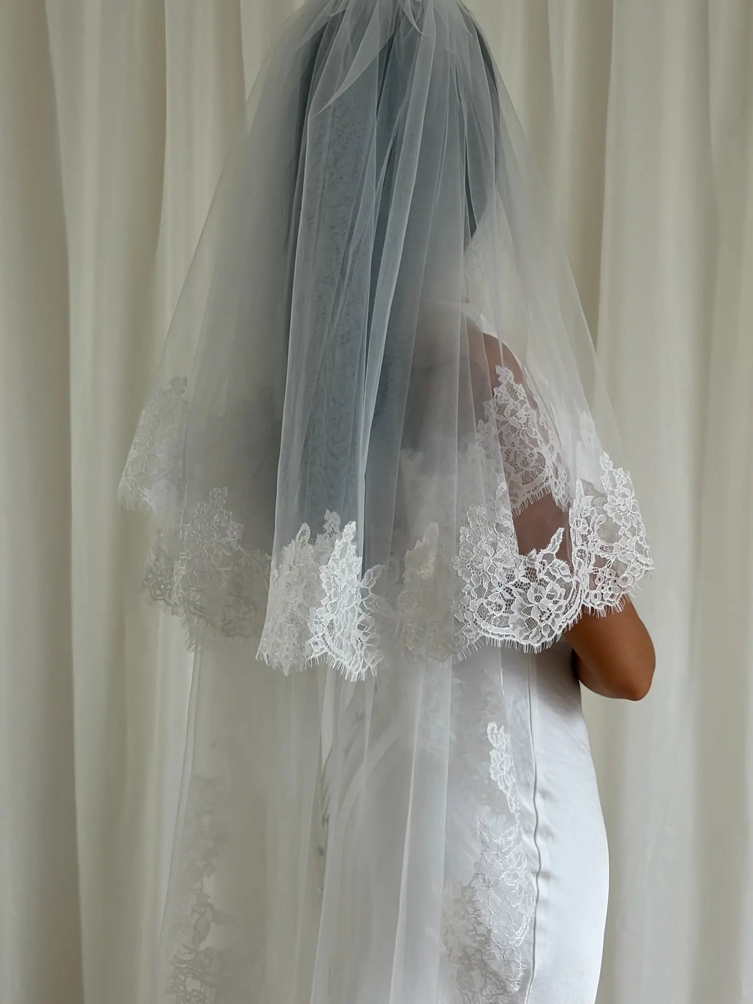 Bride wearing a white lace veil against a neutral background