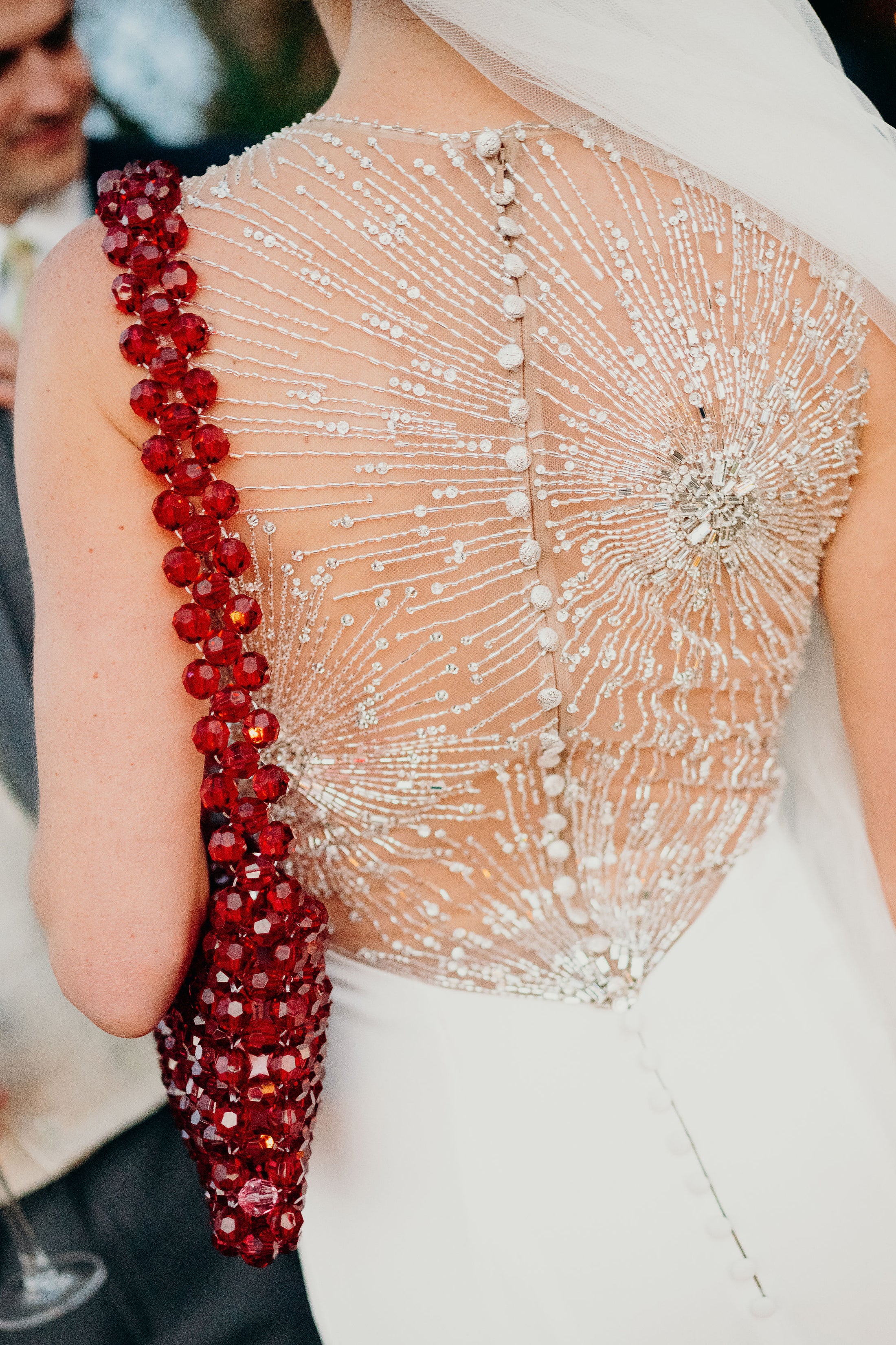 Close-up of a person wearing a white dress with intricate beadwork and red beaded bridal bag