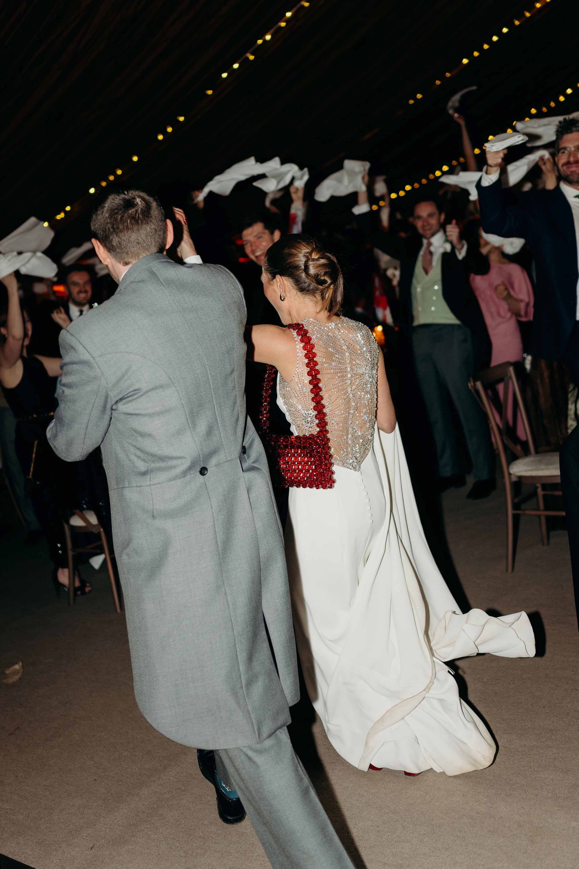 Wedding couple dancing with guests in formal attire at a reception wearing bridal bag